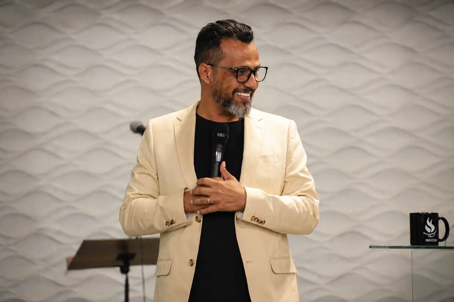 Pr. Valcenir de terno claro, com microfone na mão, sorrindo durante uma ministração na IMUCEN