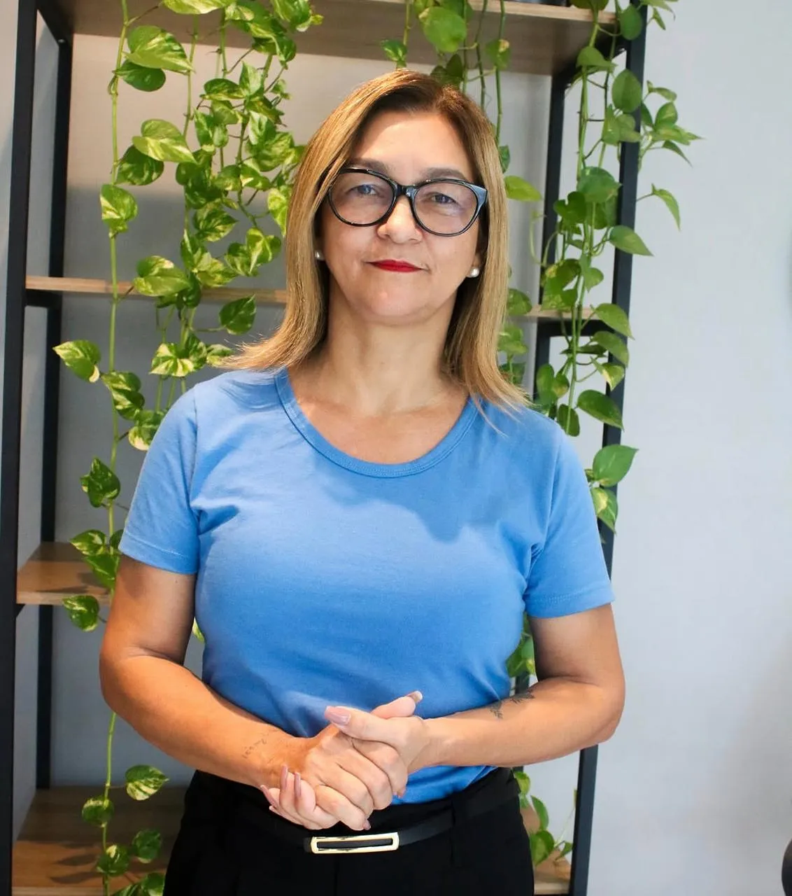 Pra. Cida de camiseta azul, mãos entrelaçadas, olhando para a câmera na sede da IMUCEN